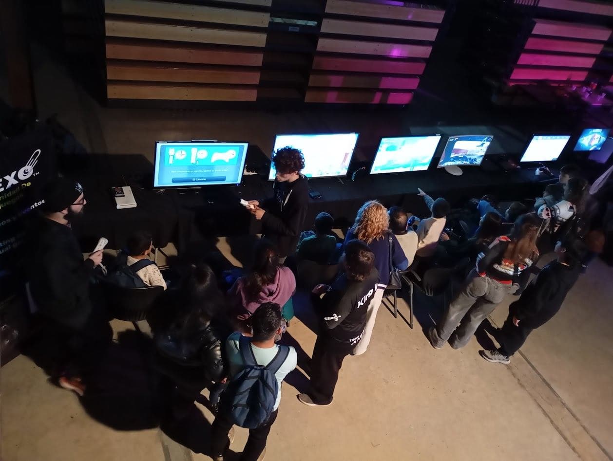 Sala oscura con una fila de pantallas y público jugando en un evento producido por Team Anexo